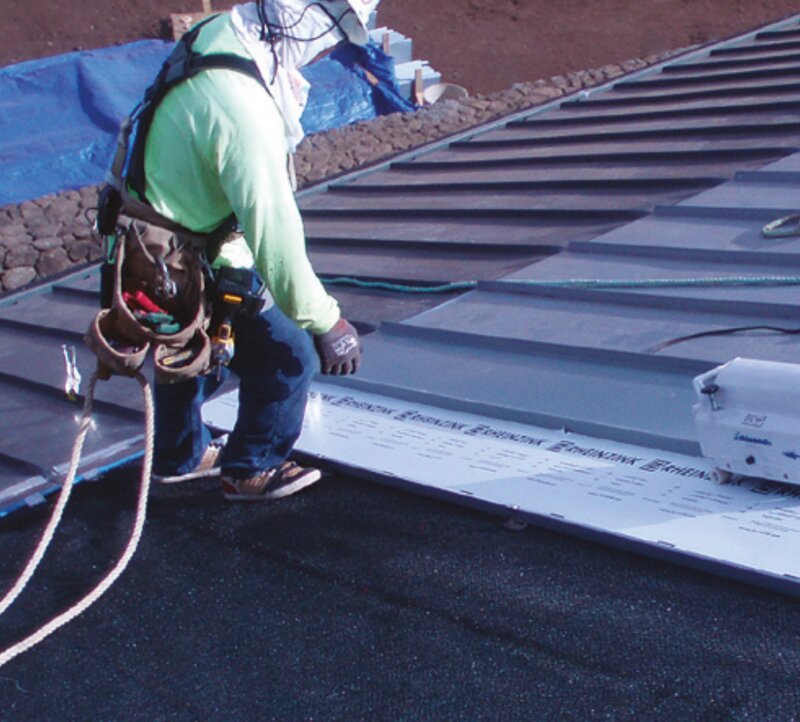 Roofing installer securing Enkamat ASV ventilation mat underlayment beneath standing seam metal roof panels
