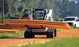 Skid steer transporting a stack of MegaDeck HD+ ground protection mats across a jobsite access road

