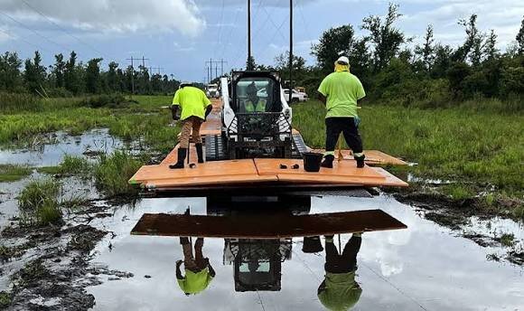 Crew using a skid steer to install MegaDeck HD+ ground protection mats over wet, flooded terrain

