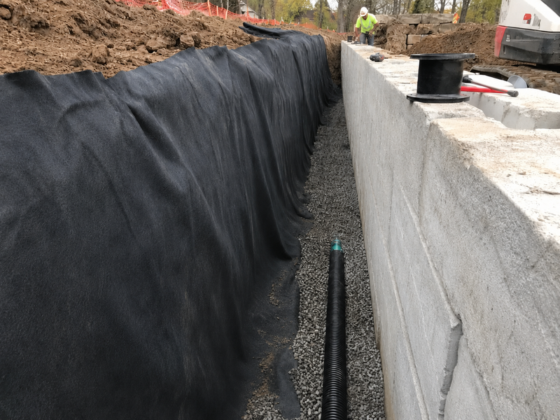 Non-woven geotextile filter fabric behind a retaining wall with gravel and drainage pipe
