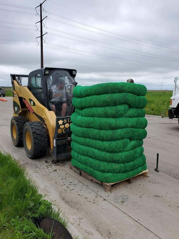 Pallet of coiled silt socks being loaded by a skid steer on a job site
