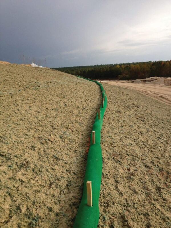 Silt sock installed as slope interruption on a sandy embankment under a stormy sky
