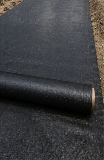 Unrolling black woven geotextile fabric across a gravel driveway subgrade
